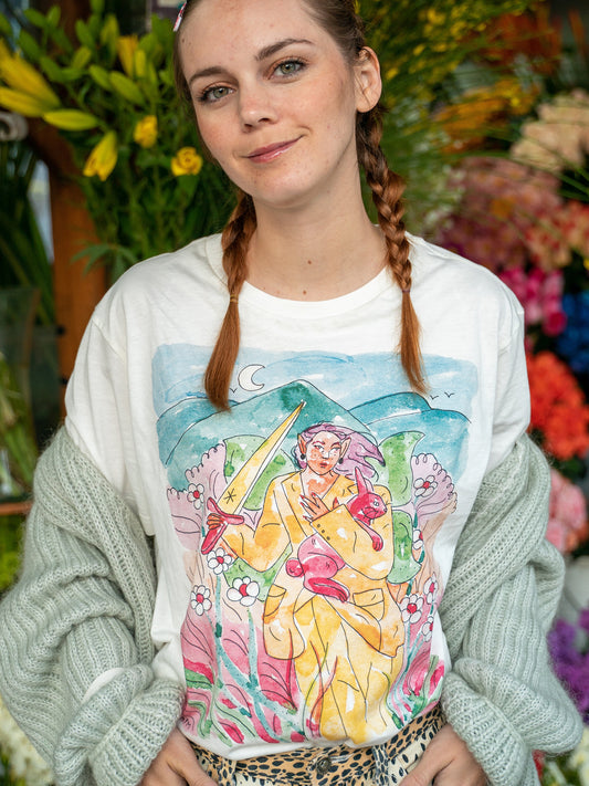 Women's short sleeve 100% cotton shirt featuring a woman warrior surrounded by highlands and nature, designed by Latino artist Ana Paula Machuca. Made in Peru